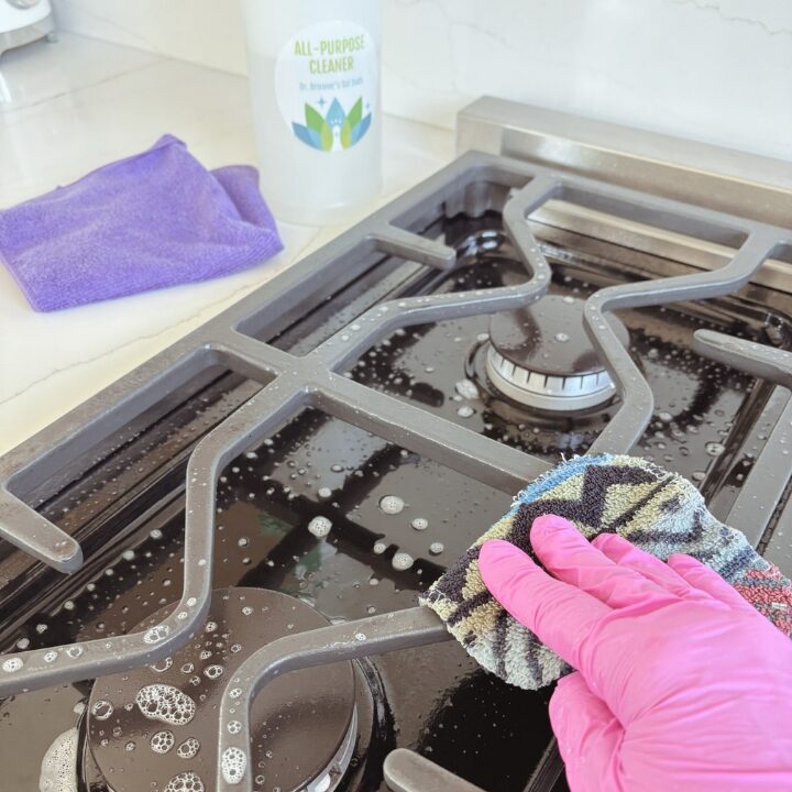 Gloved hand scrubbing a stovetop grill during recurring house cleaning in Edmonton, with a microfiber cloth and plant-based cleanser nearby