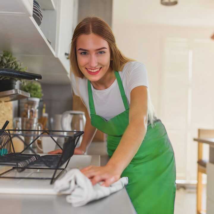 house cleaner in Edmonton wearing a green apron wiping a kitchen counter with a white towel